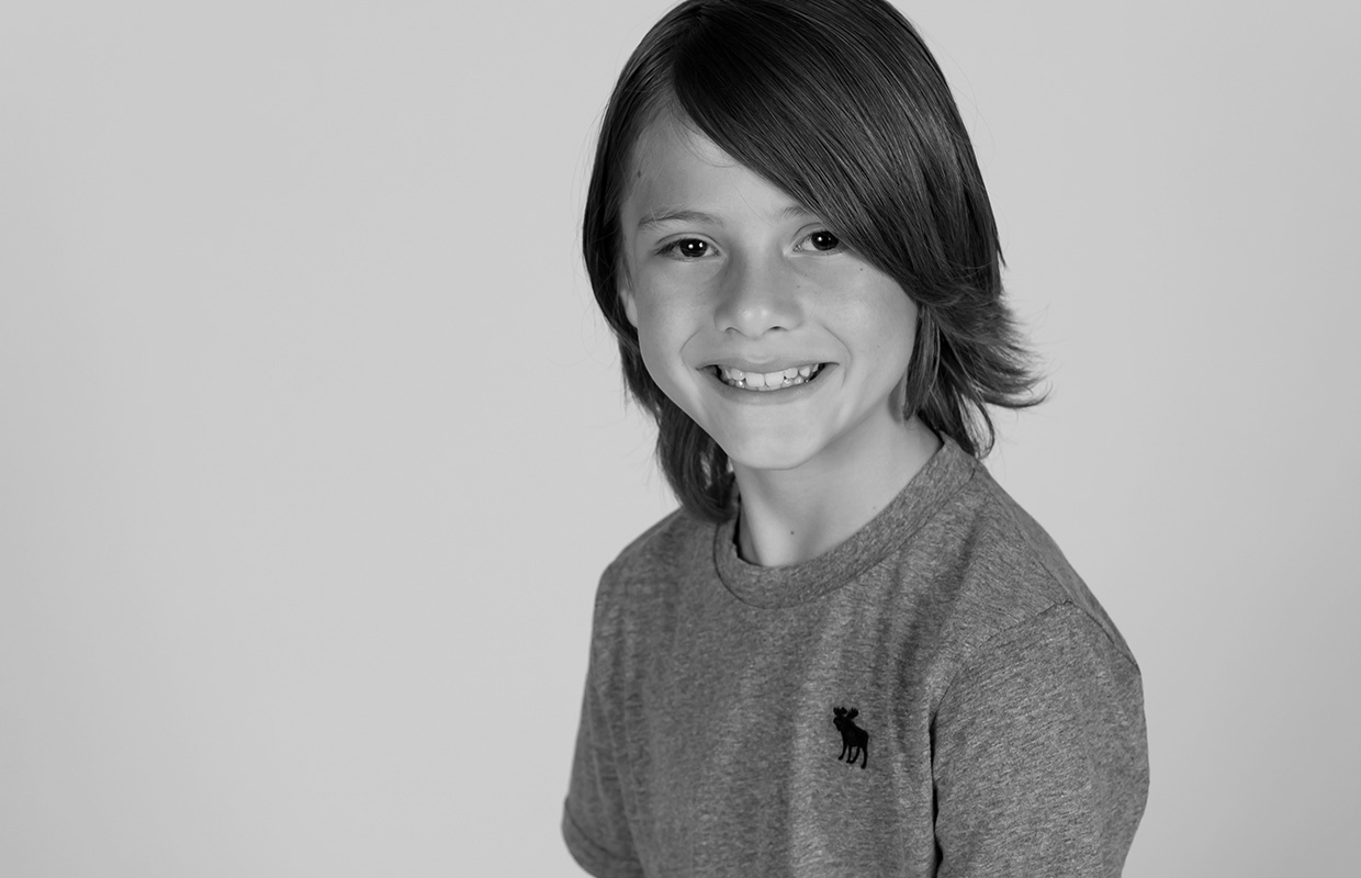 Black and white image of smiling child with shoulder-length hair and grey t-shirt