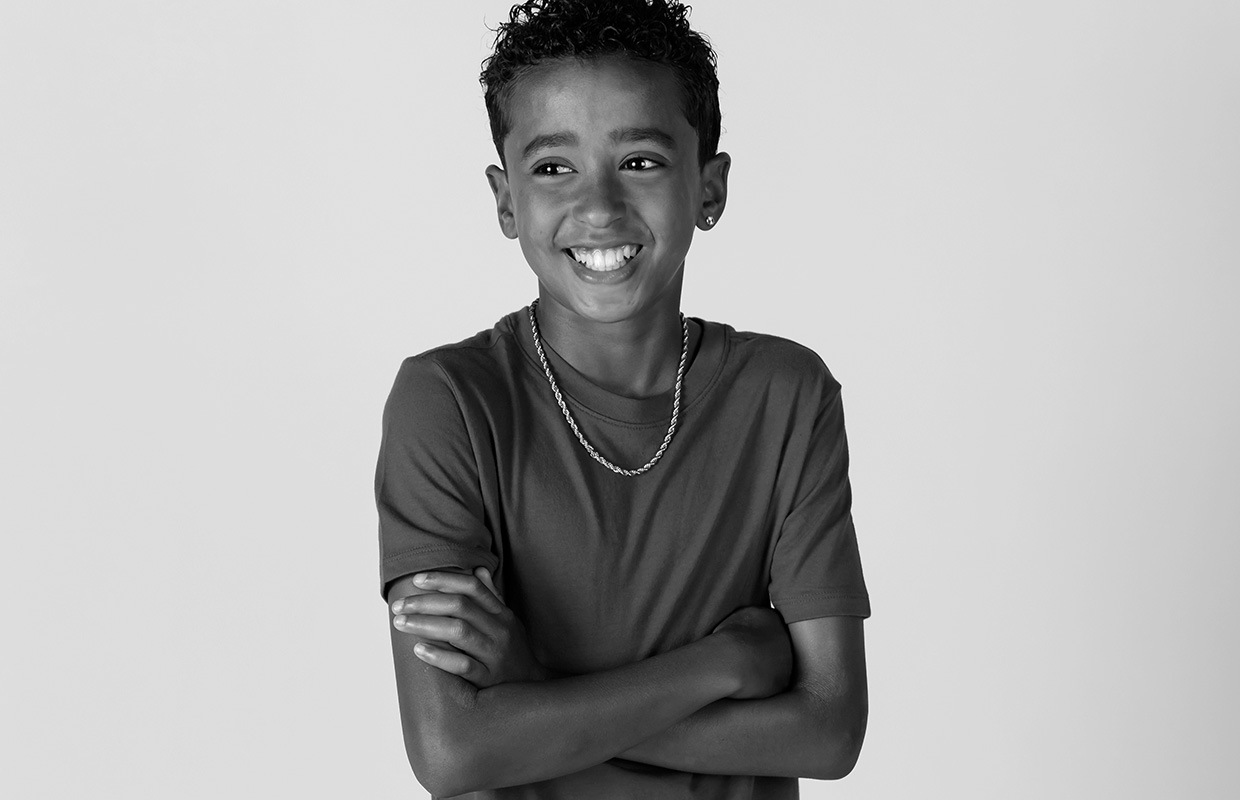 Black and white image of smiling child with braided necklace and earring