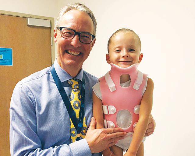 doctor posing with young girl wearing pink brace