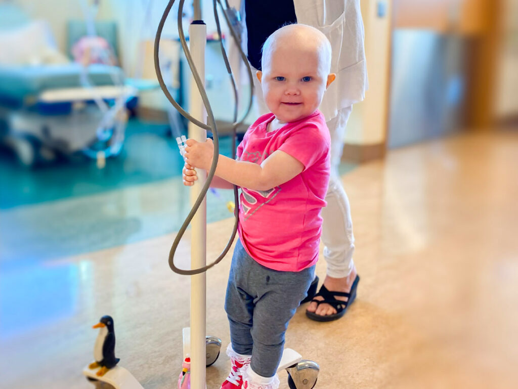 A toddler riding an IV drip down the hallways of a hospital