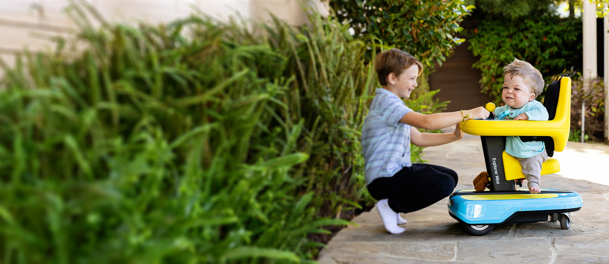 Boy interacting with young boy with achondroplasia in wheelchair/scooter device