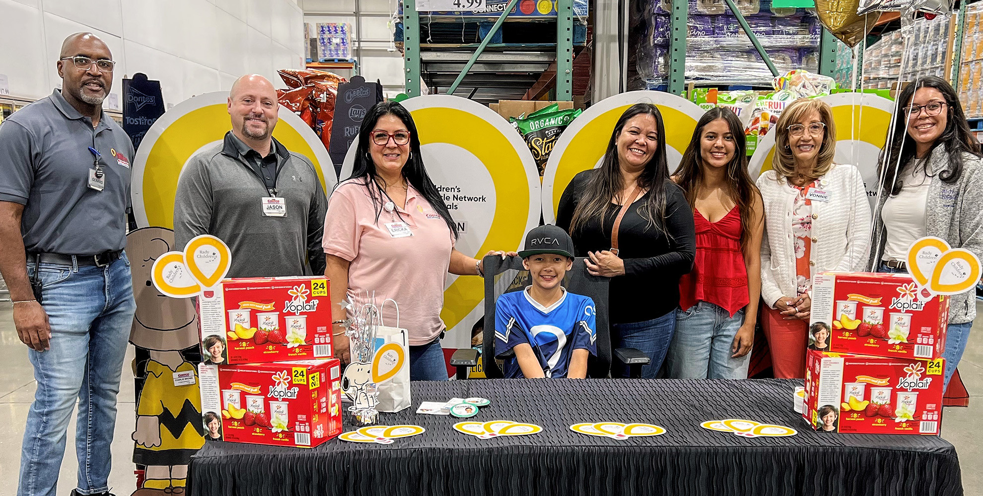 group of people standing behind patient, Landon at Costco fundraising table.