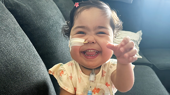 toddler girl with surgical tape covering feeding tube on her face, smiling at camera
