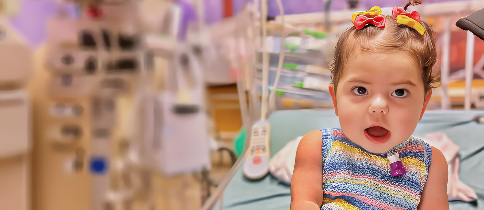toddler girl with bows in hair sitting on hospital bed