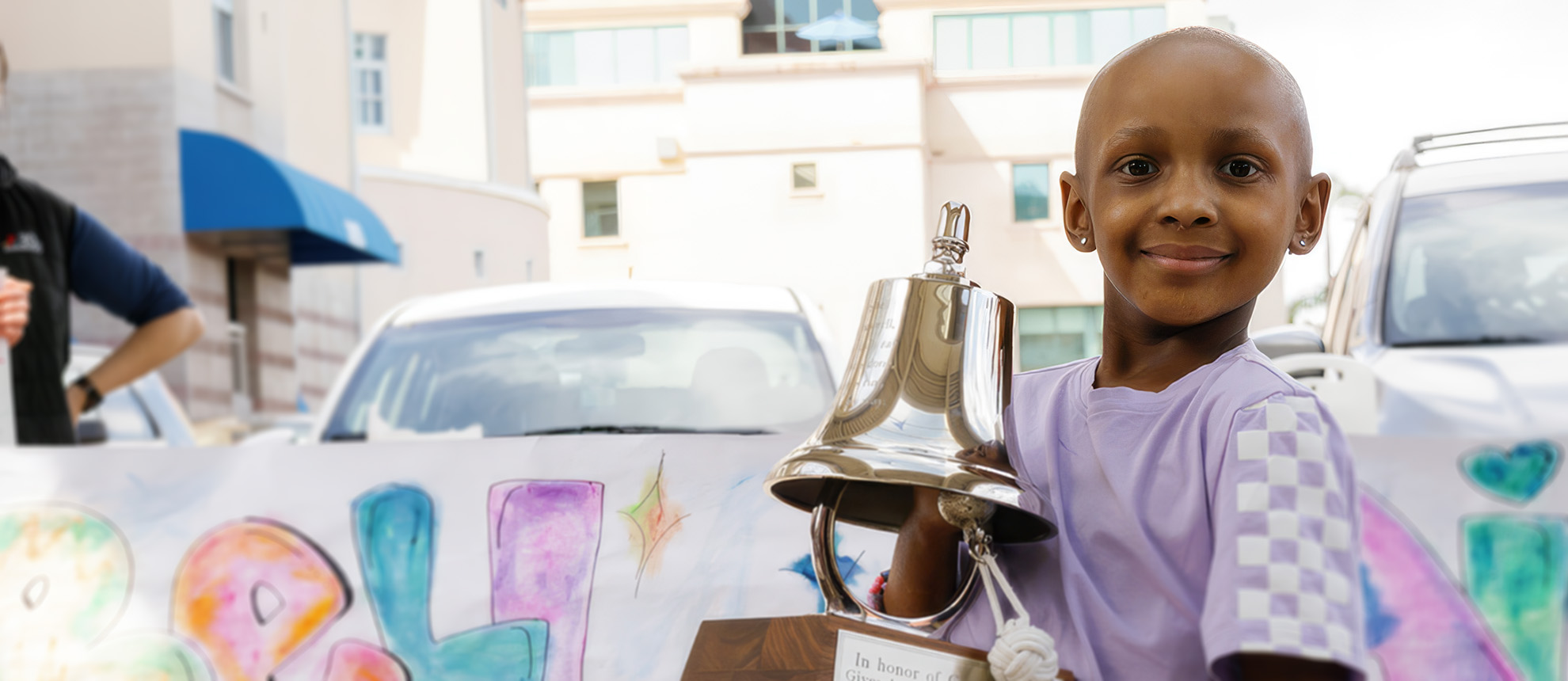 Young girl without hair, holding bell symbolizing the end of cancer treatment